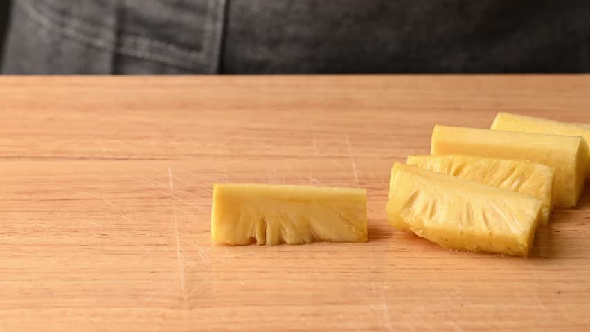 Close up of woman hands using a knife to slice fresh pineapple into small pieces on a wooden cutting board