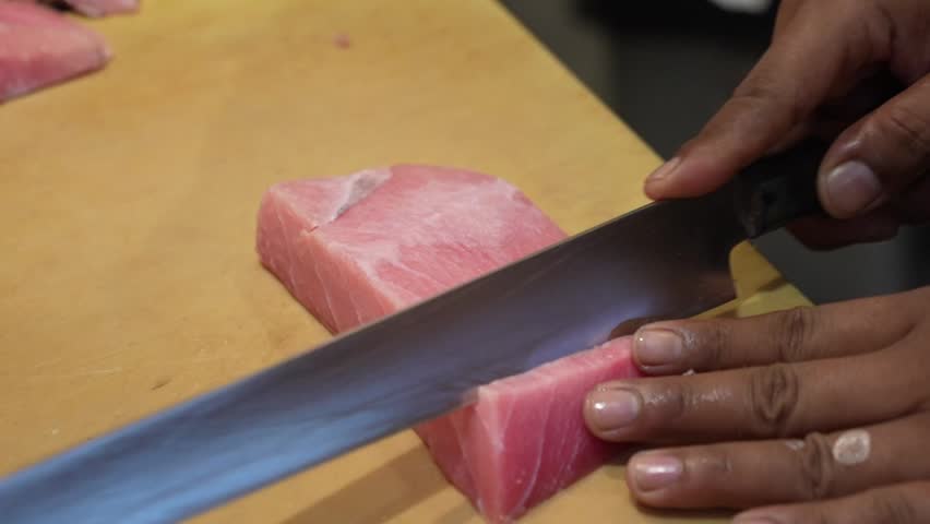 Professional chef slicing fresh tuna loin into sashimi with a sharp knife, showcasing premium seafood preparation, precision cutting, and Japanese culinary craftsmanship.