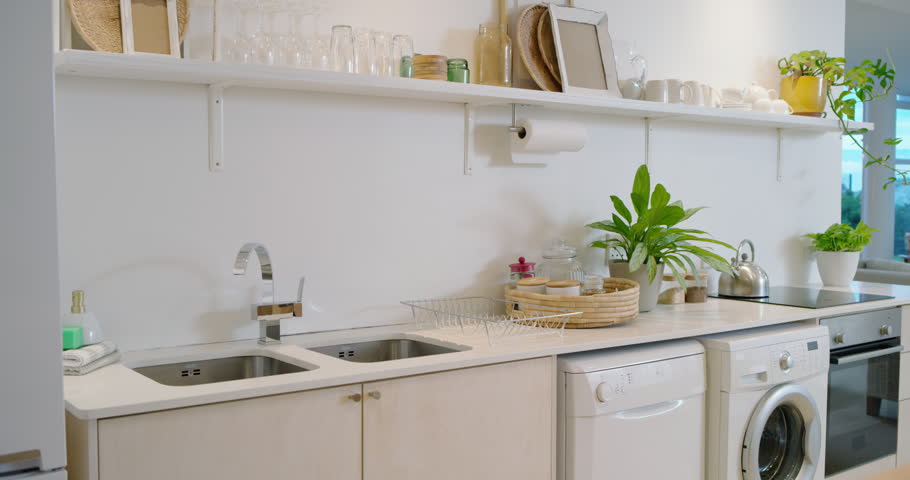 Camera is starting to pan right across kitchen countertop to reveal sink, kettle, plants and sofa. Airy, minimalist, contemporary, modern, open, spacious, neutral