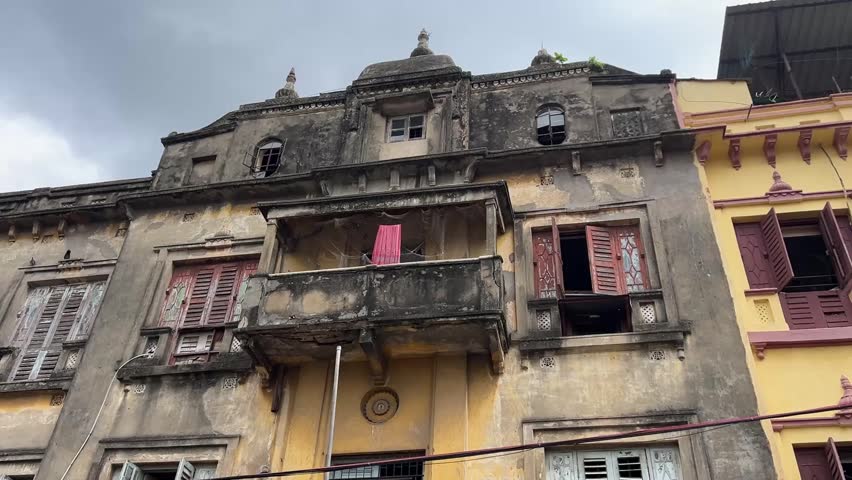 A captivating shot of a vintage colonial-style historic house in Kolkata, showcasing weathered masonry, classic green slatted windows, and timeless architectural charm, India.
