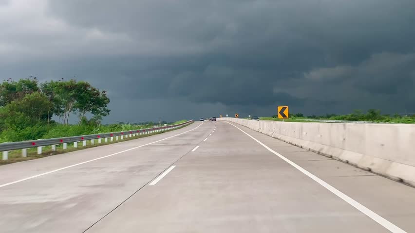 Dramatic dark storm clouds looming over a concrete highway road and open landscape during a road trip