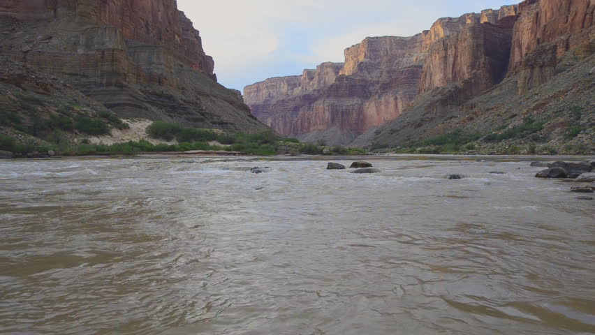 A dramatic view from river-level view of the Colorado River winding through the Grand Canyon, framed by towering red rock cliffs, rugged desert terrain, and the vast beauty of Arizona’s wilderness.