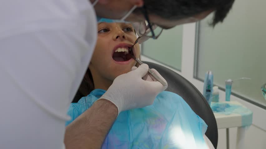 Pediatric dentist examining teeth of a brave girl sitting in dental chair