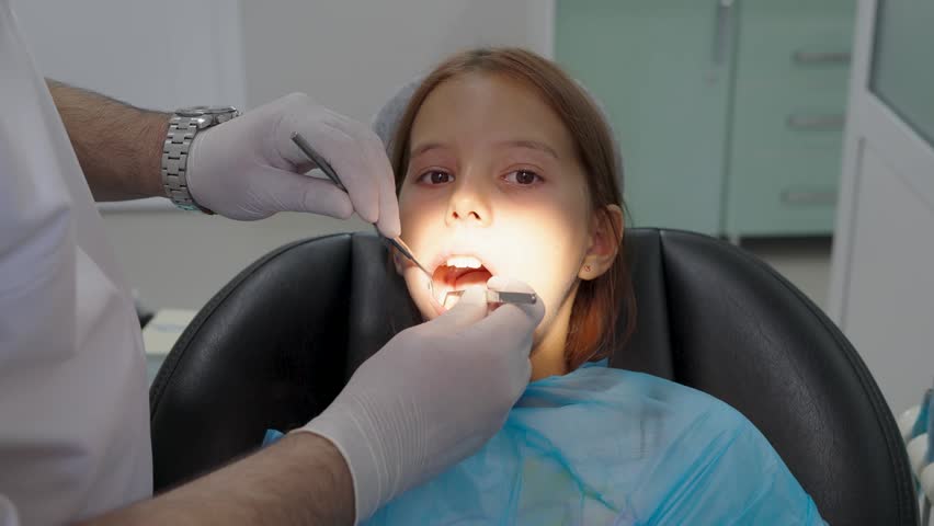 Pediatric dentist examining teeth of a brave girl sitting in dental chair