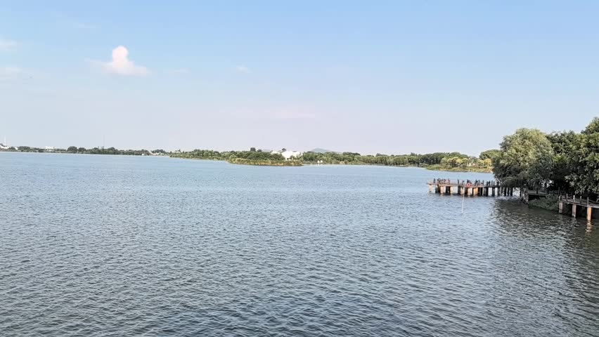A slow panoramic view moves across a wide lake with gentle ripples and a distant tree-lined shoreline under a blue sky.