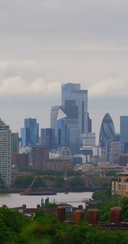 Vertical timelapse overlooking the City of London skyline with moving clouds, construction activity and boats on the River Thames.