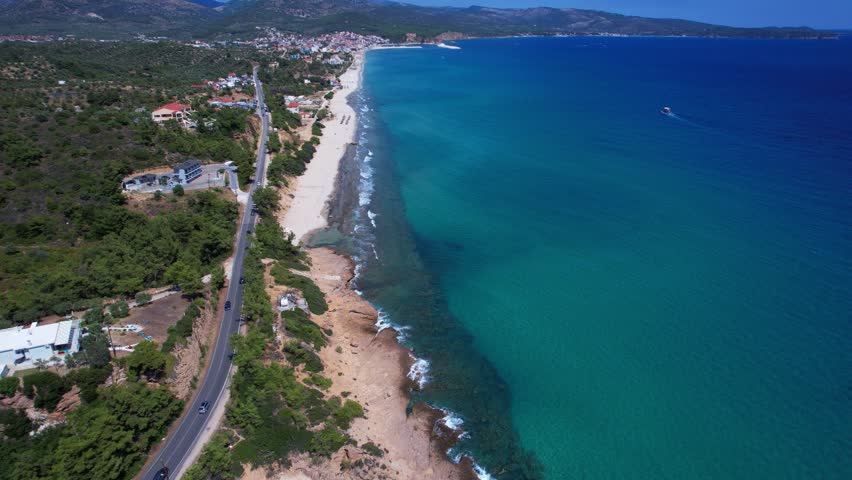 Aerial drone of a peaceful beach in Thassos, Greece, featuring transparent turquoise water, paddleboards, swimmers and a beautiful Mediterranean coastline.