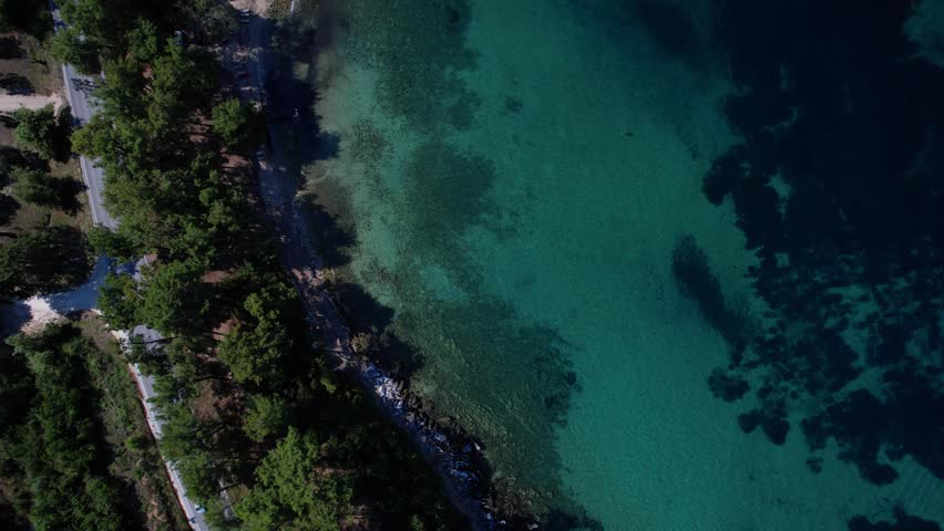 Aerial drone of a peaceful beach in Thassos, Greece, featuring transparent turquoise water, paddleboards, swimmers and a beautiful Mediterranean coastline.