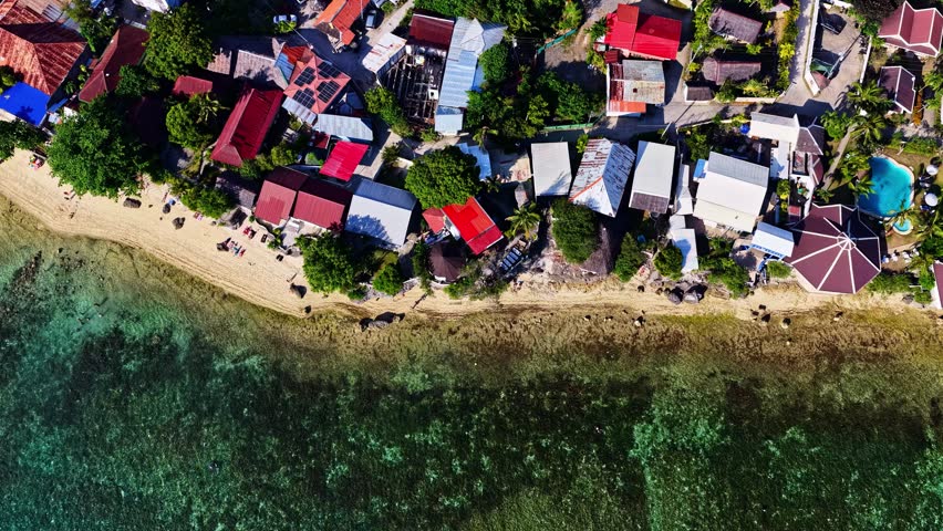 Aerial view of a coastal village with colorful rooftops, sandy beach, and clear turquoise water in the Philippines.