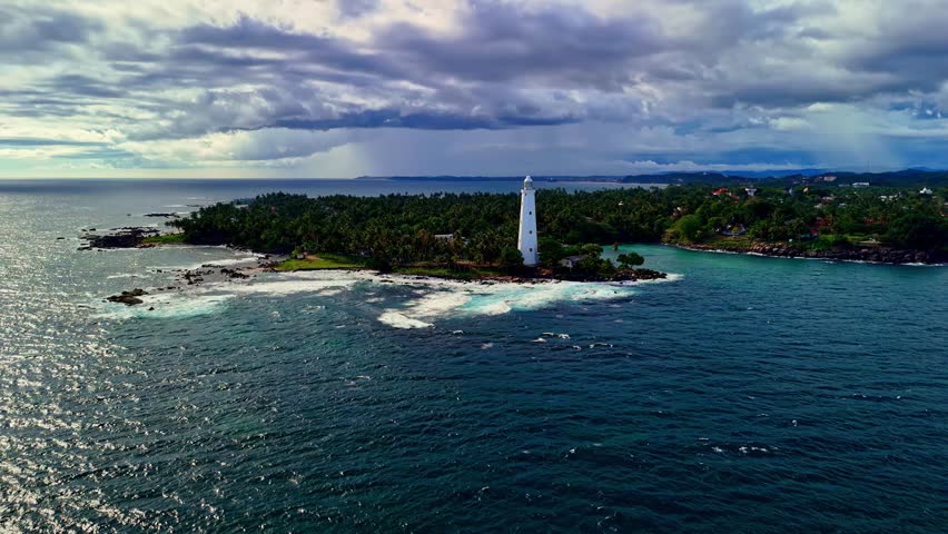 Aerial view of white lighthouse on a lush tropical island surrounded by the Indian Ocean in Sri Lanka.