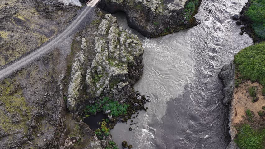 Aerial view of a river flowing through rugged volcanic rock formations and mossy terrain in the Highlands, Iceland.