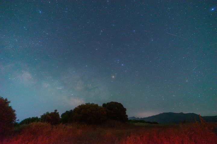Galactic core of the Milky Way moving across the night sky above a dark hill with some trees