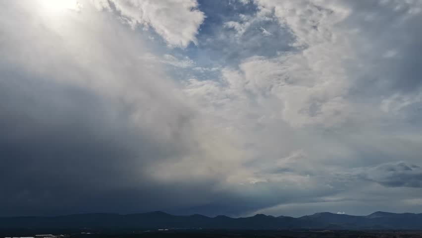 4K drone timelapse of a dark storm system forming over a mountain landscape. Thick, misty clouds and heavy atmospheric moisture move dynamically across the sky, obscuring the bright sun.
