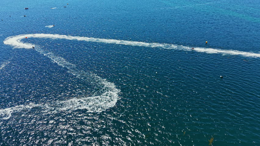 Participants in jet ski racing move quickly across the water. The scene shows several jet skis creating waves in the ocean. The event is held during a sunny day near the coast.