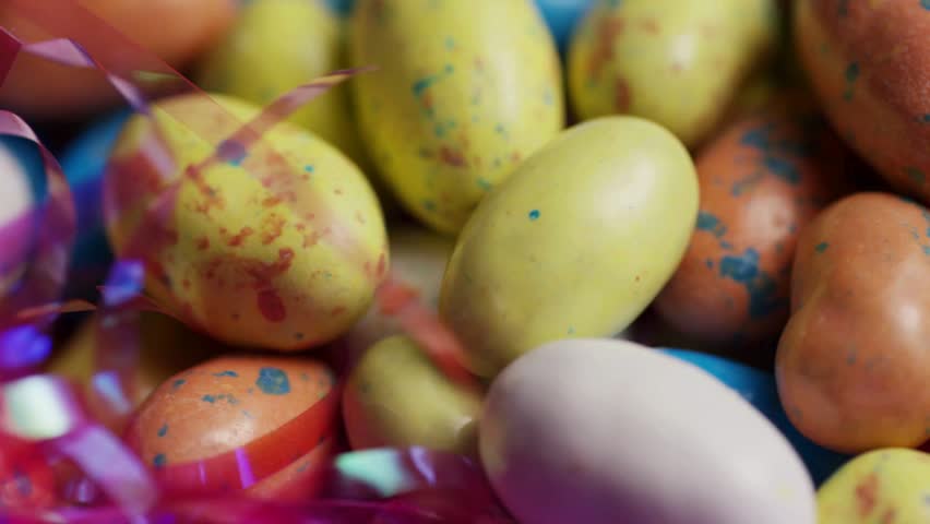 Assorted speckled pastel colored candy eggs for easter holiday nestling in pink plastic grass rotating slowly showing sweet treat