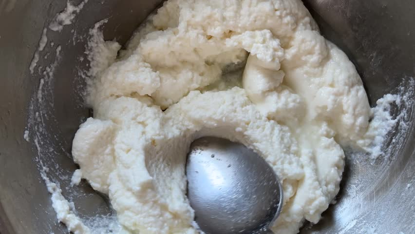 Spoon mixing fresh cottage cheese in a metal bowl for baking concept