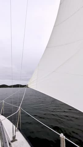 Vertical view from the deck of a sailboat looking past a full white jib sail across dark water towards distant hills on Lake Guntersville Alabama