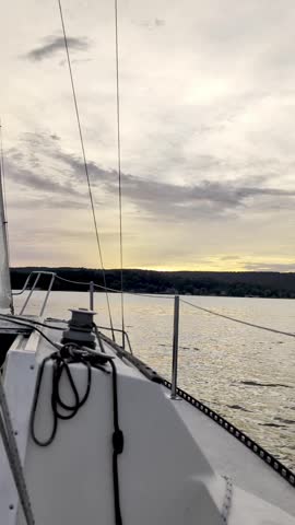 Vertical view from the deck of a sailboat featuring coiled rope lines and a winch as it sails smoothly toward a sunset shoreline on Lake Guntersville