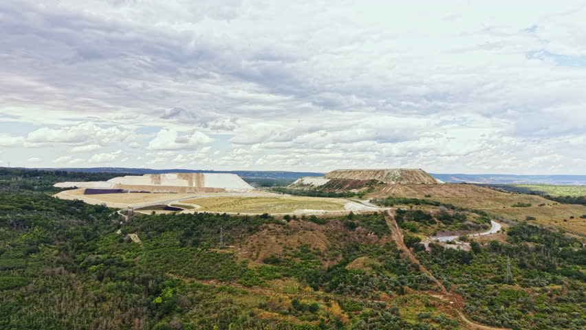 A view shows large dirt hills in a wide open space filled with trees and bushes. It