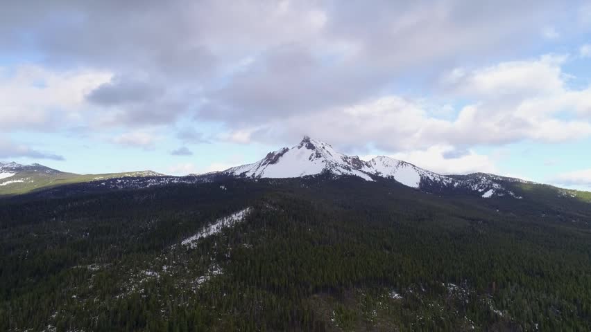 Cinematic aerial drone view reveals Mount Thielsen’s isolated, needle-like summit rising above Oregon’s Cascade forests, showcasing the extinct volcano’s dramatic alpine profile.