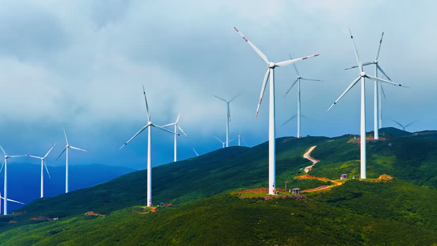 Wind turbines standing on green mountain ridge generating renewable clean energy under cloudy sky in Guilin, China.