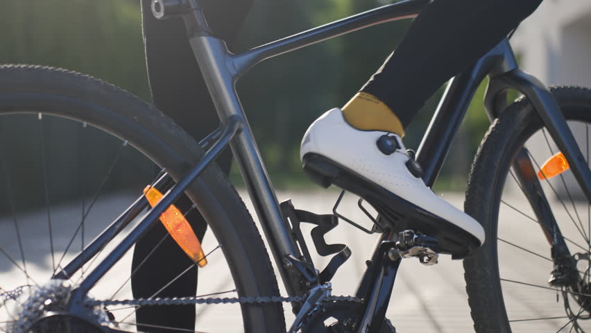 Man clips his cycling shoe into the bicycle pedal before starting a ride outdoors. Cyclist getting ready for cycling and bike training.