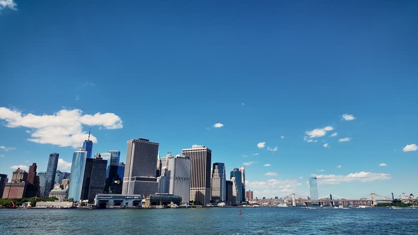 Panoramic waterfront view of the Brooklyn Bridge, Lower Manhattan skyline and a helicopter flying above New York Harbor on a clear summer day.