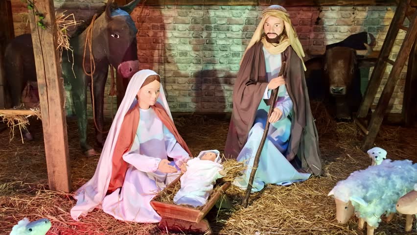 Close-up of a traditional Christmas nativity scene featuring figurines of Mary, Joseph and Baby Jesus in a manger, surrounded by a donkey, ox and sheep inside a stable decorated with straw.