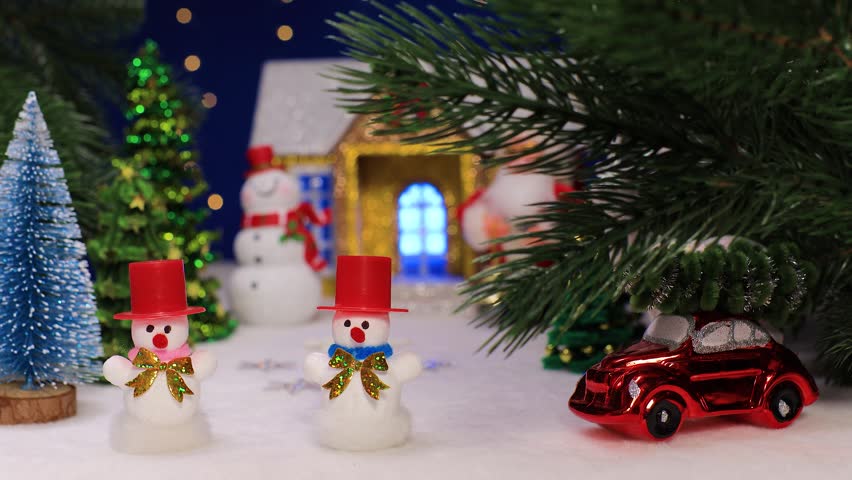 Two snowmen in red hats against the backdrop of a Christmas house with a snowman and Santa Claus