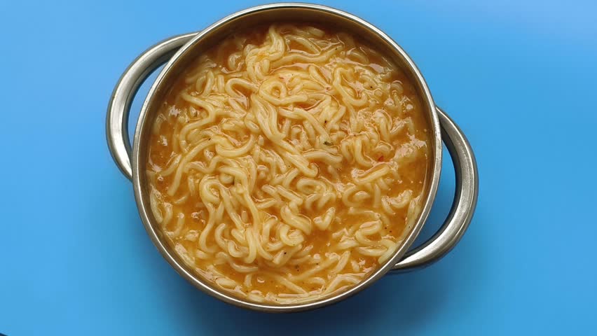 Cooked spicy chicken flavoured instant noodle or ramen Chinese style dish inside bowl served or isolated on restaurant blue table background. Closeup macro spinning or rotating top view.