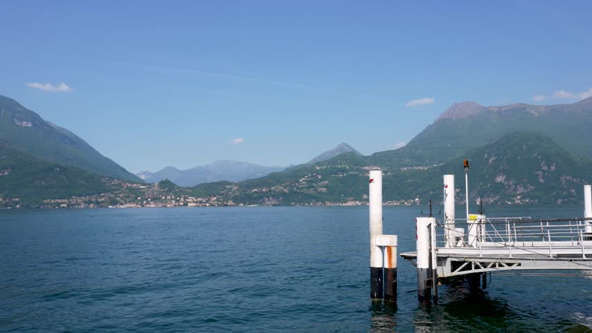 Tranquil lake scene featuring a wooden dock extending into the water, framed by green mountains and a clear blue sky, creating a serene atmosphere