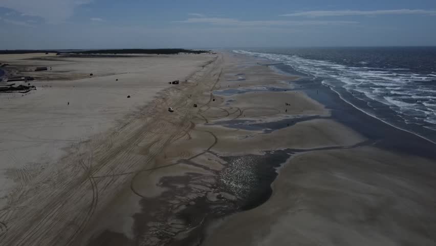 Drone view over the sandy shores and ocean tides of Caburé Beach, featuring tire tracks and off-road vehicles in Maranhão, Brazil.