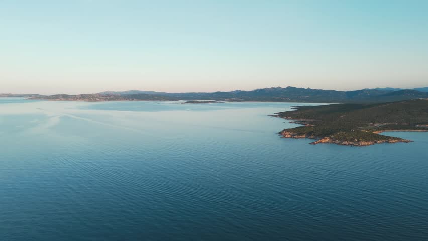 Aerial view of calm blue sea and rugged coastline at sunrise in Sardinia, Italy