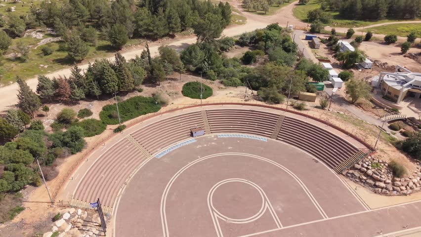 Aerial view of the Logistics Corps Memorial and Heritage Center at Tel Hadid in central Israel featuring a circular memorial amphitheater, access roads, walking paths, surrounding forest and landscaped grounds