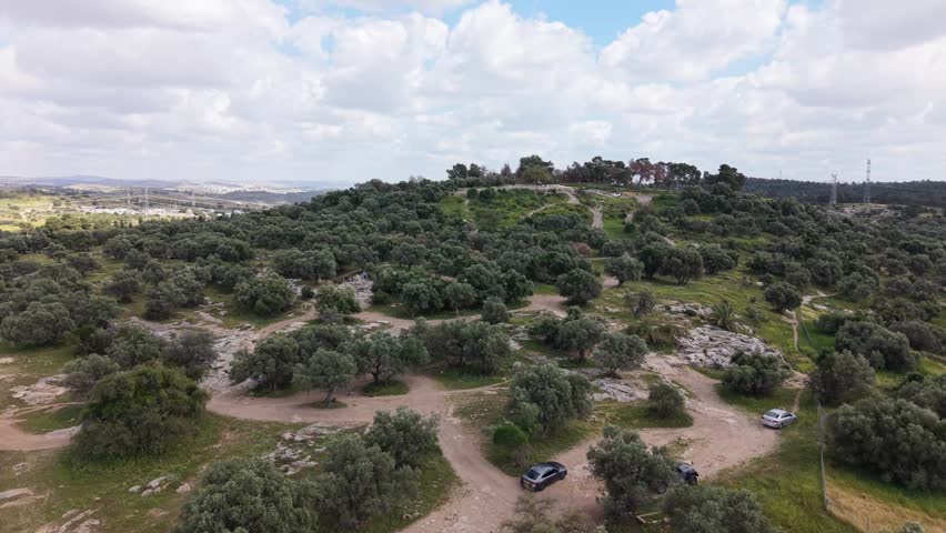 Ben Shemen Forest in Israel featuring a scenic green landscape with Mediterranean vegetation, rocky terrain, winding dirt paths and rolling hills under a cloudy sky