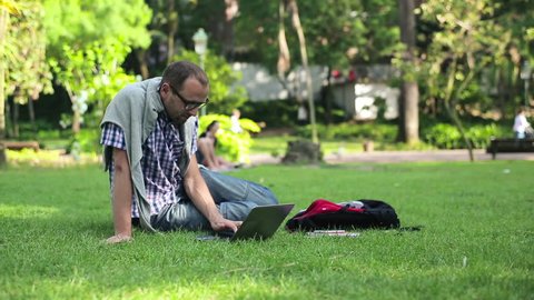 Young male student working on laptop in the park
