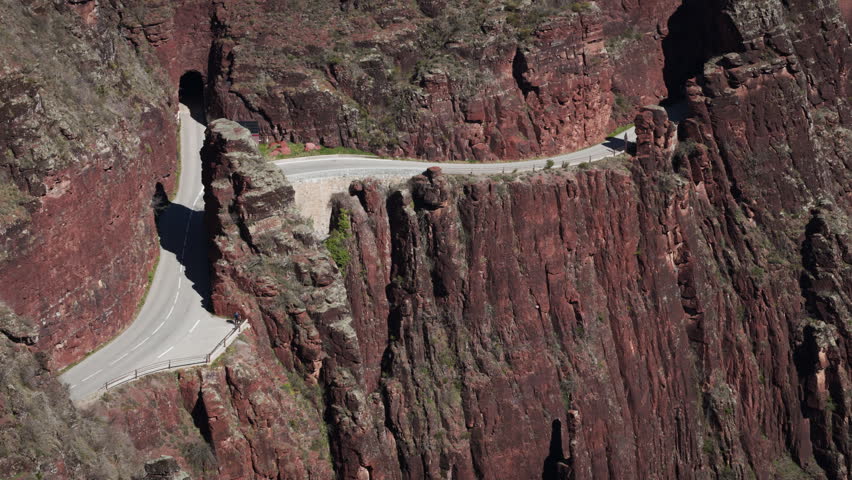 Close-up of the road through the Daluis Gorge (Gorges de Daluis) in France. A truck is emerging from a very small tunnel. Several cars are following it. The road runs along the steep cliff edge.