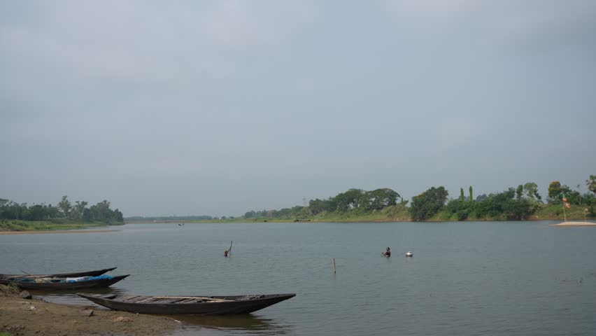Two boats are moored in the river, and two people are fishing in the distance.