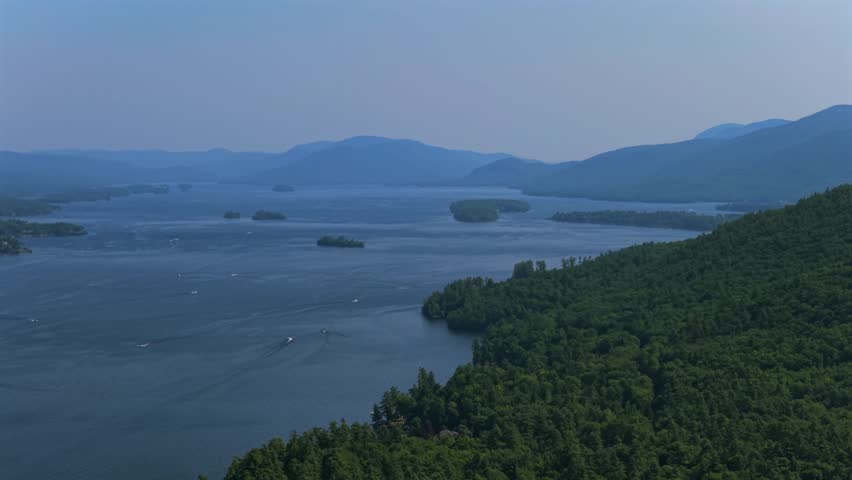 Lake George Adirondack Mountains July boats Boating aerial drone Up State New York Town of Lake George landscape harbor view Assembly Point spring summer sunny morning blue sky pan left motion
