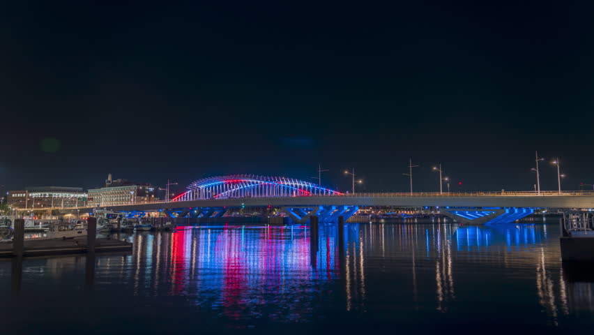 Timelapse of Bridge illuminated with red and blue lights at night.