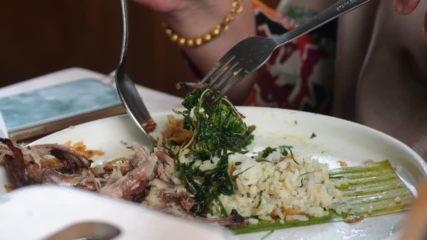 An Indonesian woman eating fried rice or Nasi Goreng (indonesian) with spoon and fork at a restaurant
