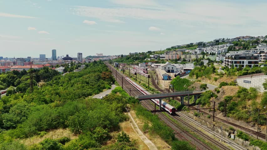 Aerial view of a passenger train entering Bratislava, Slovakia, with the main railway yard, Bratislava Castle on the horizon and the city