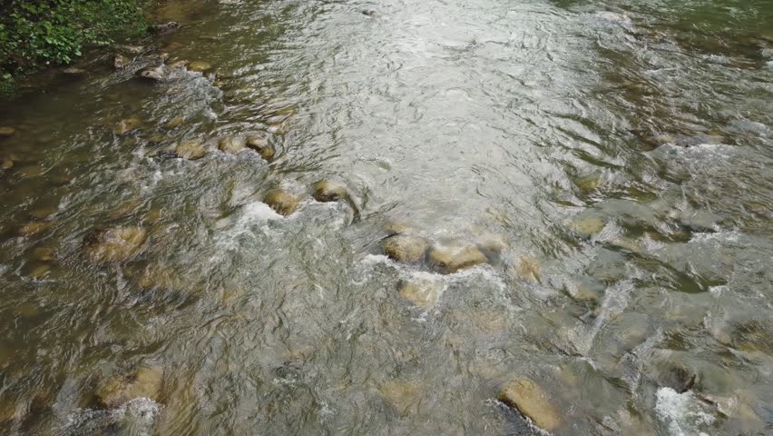Water flow in a mountain river with narrow footbridge made with halved wooden logs at autumn overcast morning, aerial view while moving forward against the current at low altitude
