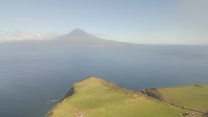 Aerial Reveal, Lighthouse of Ribeirinha on Faial Island, Azores, Portugal, overlooking the Atlantic Ocean with Pico Mountain visible across the water