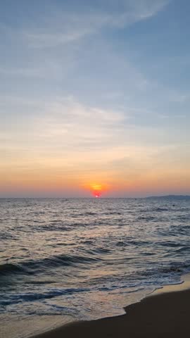 Vibrant orange sunset over calm ocean waves on sandy beach horizon
