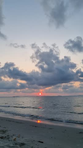 Morning red sunrise over calm sea waves at sandy beach with dramatic cloudy sky