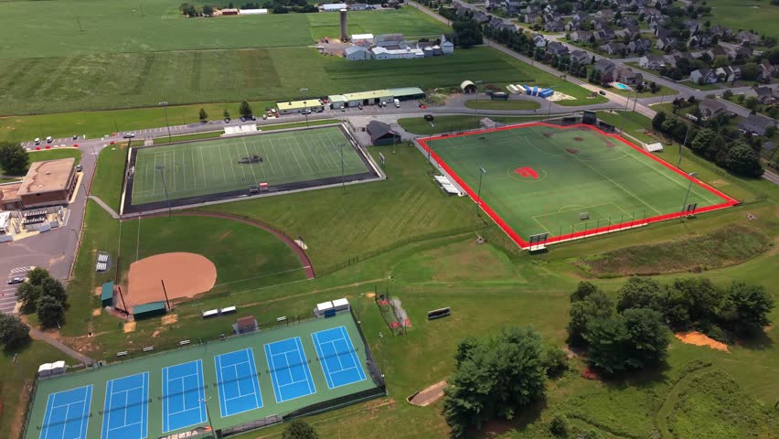 Aerial view of suburban high school athletic fields featuring tennis courts swimming pool and parking facilities