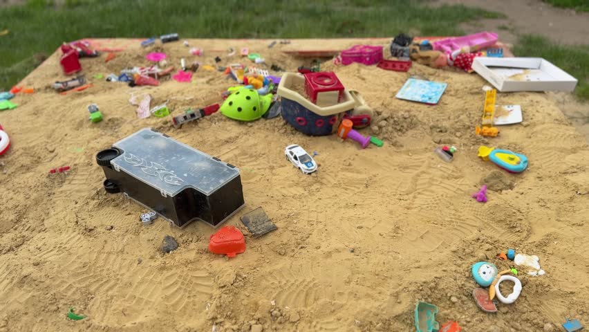 A colorful collection of children’s toys is scattered across a sandy playground. A toy boat, miniature cars, plastic shovels, buckets, building pieces, and play accessories create a lively scene of outdoor childhood activity. This image belongs to the categories of childhood, playground, outdoor recreation, education, family lifestyle, and children’s entertainment. It represents creative play, imagination, learning through games, summer fun, social development, messy play, active childhood, leisure, exploration, sensory activities, and joyful time spent outdoors.