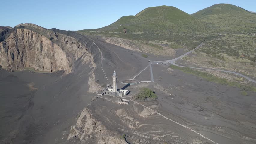 Aerial view of lighthouse surrounded by volcanic landscape and rugged hills in daylight