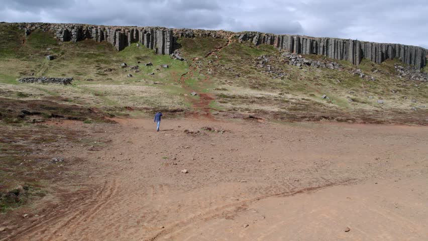Lone man walking along a trail toward the Gerduberg cliffs, an impressive row of hexagonal basalt columns on the Snafellsnes peninsula, Iceland